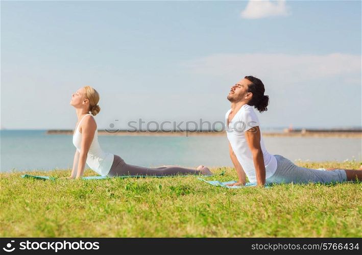 fitness, sport, friendship and lifestyle concept - smiling couple making yoga exercises lying on mats outdoors
