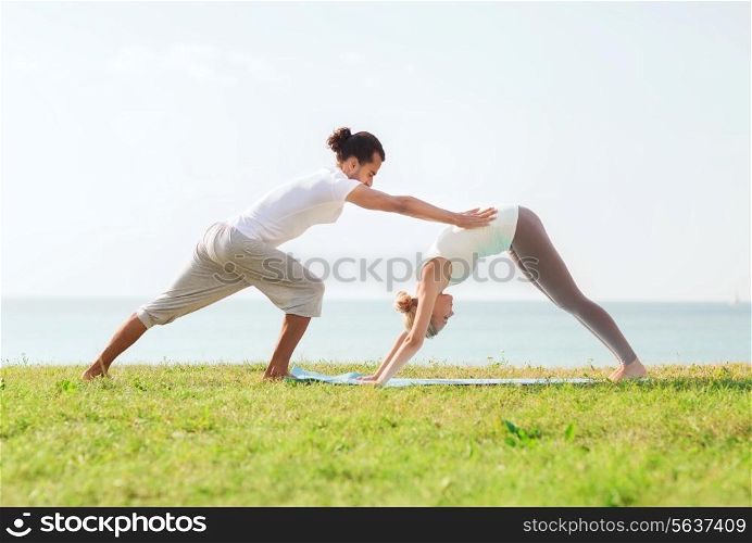 fitness, sport, friendship and lifestyle concept - smiling couple making yoga exercises on mat outdoors