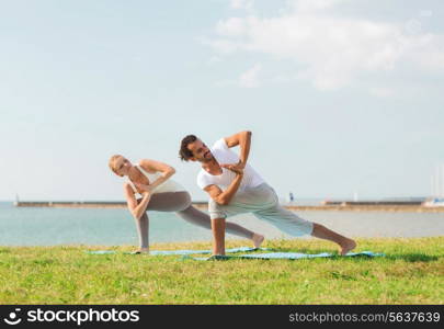 fitness, sport, friendship and lifestyle concept - smiling couple making yoga exercises on mats outdoors