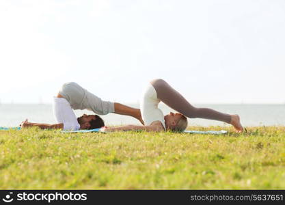 fitness, sport, friendship and lifestyle concept - smiling couple making yoga exercises on mats outdoors