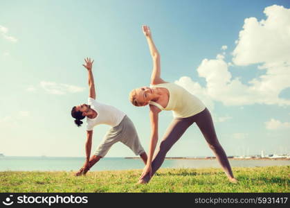 fitness, sport, friendship and lifestyle concept - smiling couple making yoga exercises outdoors