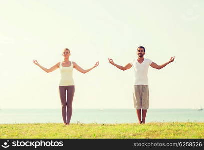 fitness, sport, friendship and lifestyle concept - smiling couple making yoga exercises outdoors