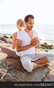 fitness, sport, friendship and lifestyle concept - smiling couple making yoga exercises sitting outdoors