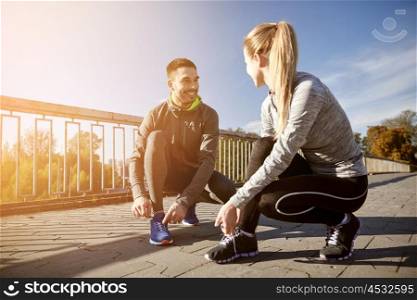 fitness, sport, friendship and lifestyle concept - smiling couple tying shoelaces outdoors