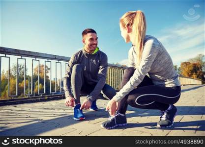 fitness, sport, friendship and lifestyle concept - smiling couple tying shoelaces outdoors. smiling couple tying shoelaces outdoors