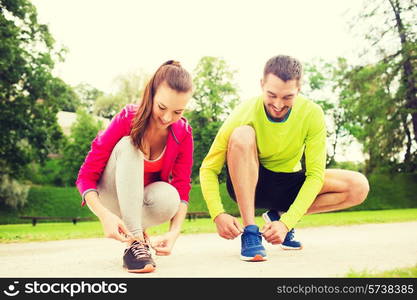 fitness, sport, friendship and lifestyle concept - smiling couple tying shoelaces outdoors