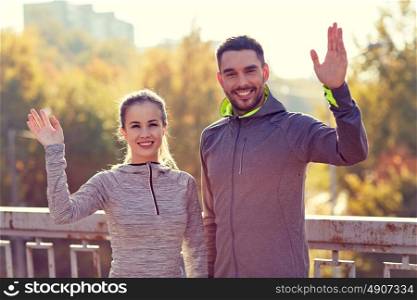 fitness, sport, friendship and lifestyle concept - smiling couple waving hand outdoors. smiling couple waving hand outdoors