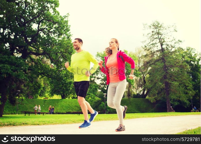 fitness, sport, friendship and lifestyle concept - smiling couple with earphones running outdoors