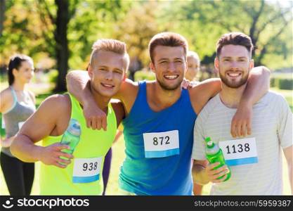 fitness, sport, friendship, marathon and healthy lifestyle concept - group of happy teenage friends or sportsmen with racing badge numbers and water bottles outdoors
