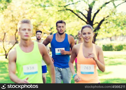 fitness, sport, friendship, race and healthy lifestyle concept - group of happy teenage friends or sportsmen running marathon with badge numbers outdoors