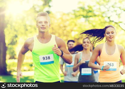 fitness, sport, friendship, race and healthy lifestyle concept - group of happy teenage friends or sportsmen running marathon with badge numbers outdoors