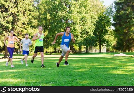 fitness, sport, friendship, race and healthy lifestyle concept - group of happy teenage friends or sportsmen running marathon with badge numbers outdoors