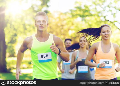 fitness, sport, friendship, race and healthy lifestyle concept - group of happy teenage friends or sportsmen running marathon with badge numbers outdoors