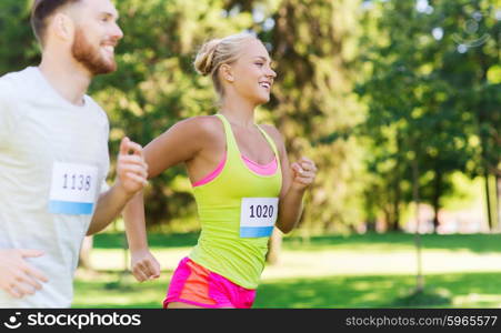 fitness, sport, friendship, race and healthy lifestyle concept - happy teenage friends or sportsmen couple running marathon with badge numbers outdoors