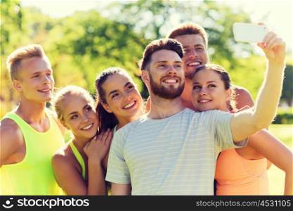 fitness, sport, friendship, technology and healthy lifestyle concept - group of happy teenage friends taking selfie with smartphone outdoors