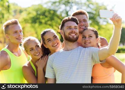 fitness, sport, friendship, technology and healthy lifestyle concept - group of happy teenage friends taking selfie with smartphone outdoors