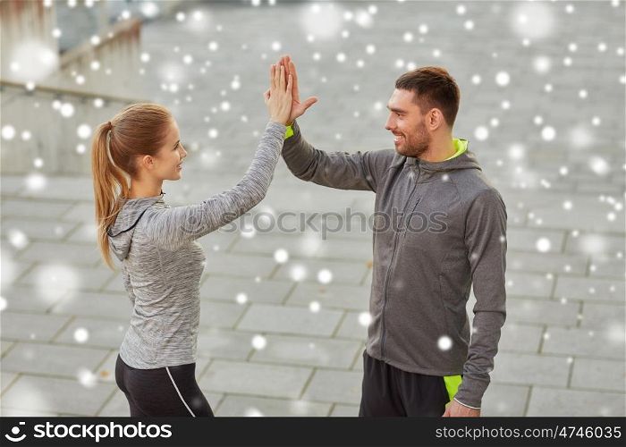 fitness, sport, gesture, people and success concept - happy couple giving high five outdoors over snow