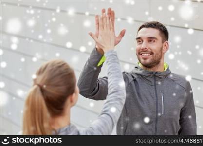 fitness, sport, gesture, people and success concept - happy couple giving high five outdoors over snow