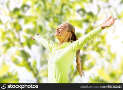 fitness, sport, happiness and people concept - happy woman raising hands over green tree leaves background