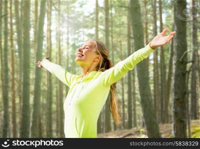 fitness, sport, happiness and people concept - happy woman raising hands over woods background
