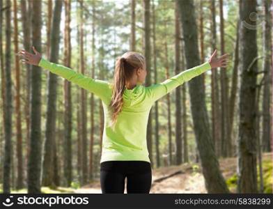 fitness, sport, happiness and people concept - happy woman raising hands over woods background from back