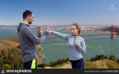 fitness, sport, martial arts and people concept - happy woman with personal trainer working on strike over golden gate bridge in san francisco bay background. happy woman with coach working on strike outdoors. happy woman with coach working on strike outdoors