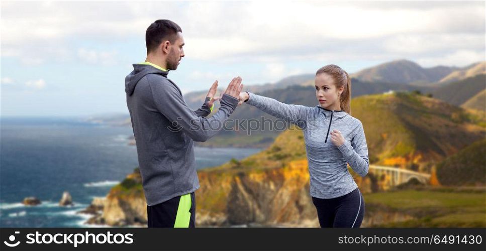 fitness, sport, martial arts and people concept - happy woman with personal trainer working on strike over bixby creek bridge on big sur coast of california background. happy woman with coach working on strike outdoors. happy woman with coach working on strike outdoors