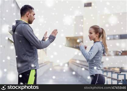 fitness, sport, martial arts, self-defense and people concept - woman with personal trainer working out strike outdoors over snow