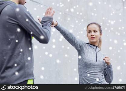 fitness, sport, martial arts, self-defense and people concept - woman with personal trainer working out strike outdoors over snow