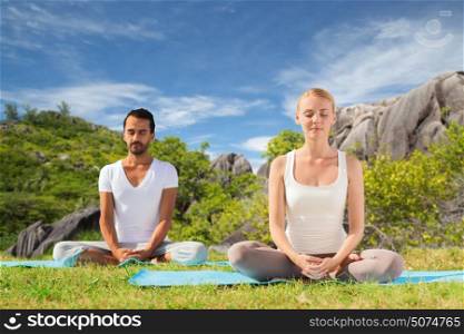 fitness, sport, meditation and people concept - happy couple doing yoga and meditating outdoors over natural background. happy couple doing yoga and meditating outdoors