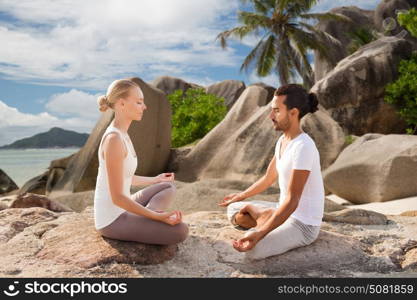 fitness, sport, meditation and people concept - happy couple doing yoga and meditating outdoors over tropical natural background. happy couple doing yoga and meditating outdoors