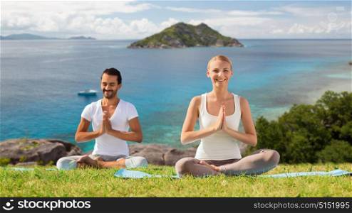 fitness, sport, meditation and people concept - happy couple doing yoga and meditating outdoors over natural background and sea. happy couple doing yoga and meditating outdoors