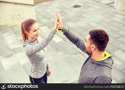 fitness, sport, people and gesture concept - smiling couple making high five on city street. smiling couple making high five on city street