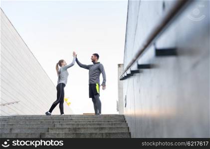 fitness, sport, people and gesture concept - smiling couple making high five on city street