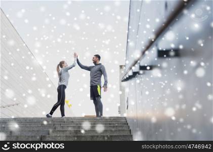fitness, sport, people and gesture concept - smiling couple of sportsmen making high five on city street over snow