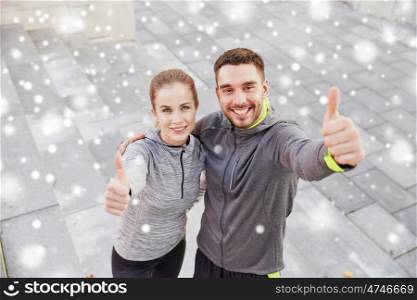 fitness, sport, people and gesture concept - smiling couple of sportsmen outdoors showing thumbs up on city street stairs over snow