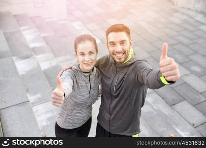 fitness, sport, people and gesture concept - smiling couple outdoors showing thumbs up on city street stairs
