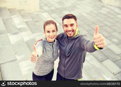 fitness, sport, people and gesture concept - smiling couple outdoors showing thumbs up on city street stairs. smiling couple showing thumbs up on city street