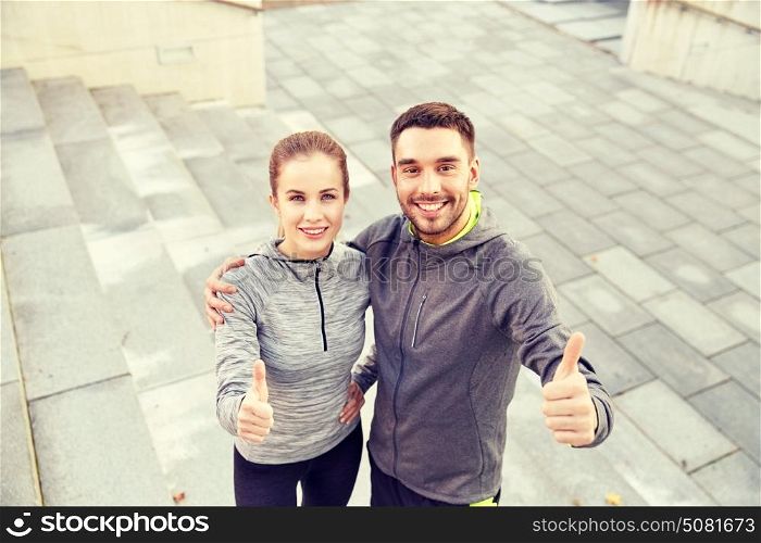 fitness, sport, people and gesture concept - smiling couple outdoors showing thumbs up on city street stairs. smiling couple showing thumbs up on city street