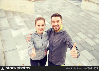 fitness, sport, people and gesture concept - smiling couple outdoors showing thumbs up on city street stairs. smiling couple showing thumbs up on city street