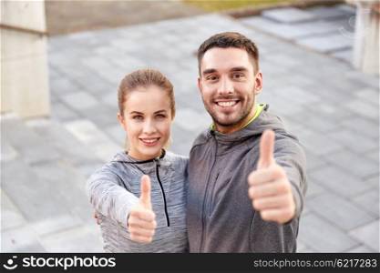 fitness, sport, people and gesture concept - smiling couple outdoors showing thumbs up on city street stairs