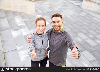 fitness, sport, people and gesture concept - smiling couple outdoors showing thumbs up on city street stairs