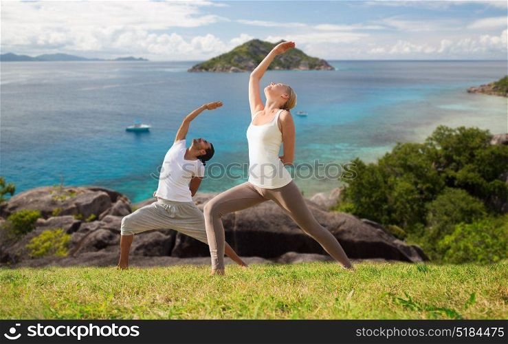 fitness, sport, people and healthy lifestyle concept - couple doing yoga in warrior pose over natural background and sea. couple doing yoga over natural background and sea