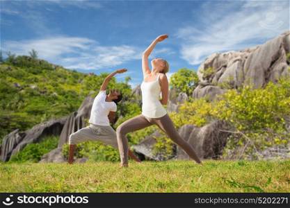 fitness, sport, people and healthy lifestyle concept - couple doing yoga in warrior pose on beach over natural background. couple doing yoga exercises on beach