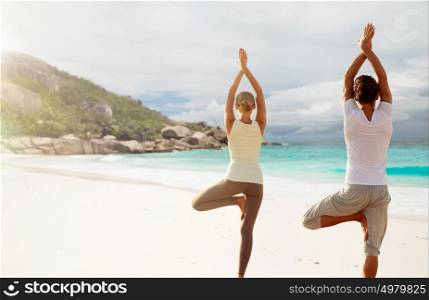 fitness, sport, people and healthy lifestyle concept - couple making yoga in tree pose over exotic beach background from back . young woman making yoga exercises on beach
