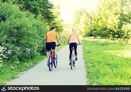 fitness, sport, people and healthy lifestyle concept - happy couple riding bicycle outdoors at summer from back