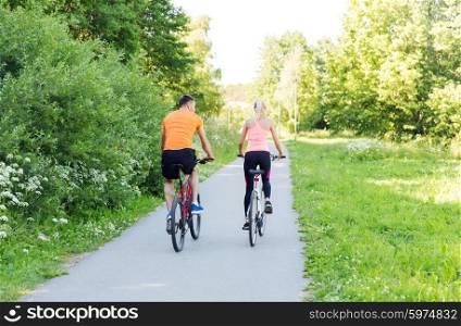 fitness, sport, people and healthy lifestyle concept - happy couple riding bicycle outdoors at summer from back