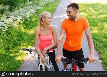fitness, sport, people and healthy lifestyle concept - happy couple riding bicycle outdoors at summer