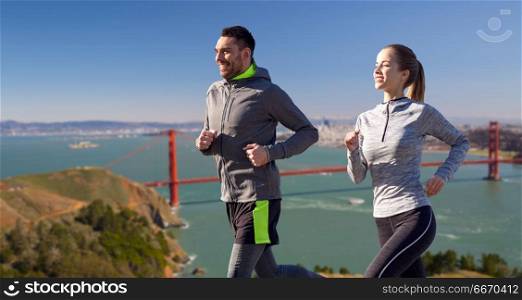fitness, sport, people and healthy lifestyle concept - happy couple running over golden gate bridge in san francisco bay background. happy couple running over golden gate bridge. happy couple running over golden gate bridge