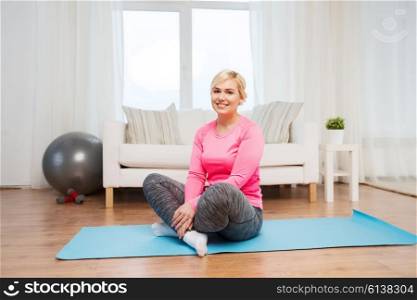 fitness, sport, people and healthy lifestyle concept - happy plus size woman sitting on mat at home